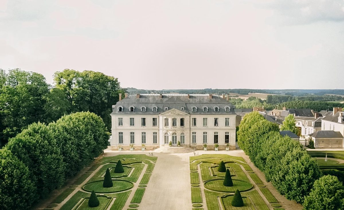 Aerial drone view of Château du Grand-Lucé neoclassical façade with formal French gardens, geometric boxwood hedges and the Loire Valley countryside beyond — Loire Valley, France