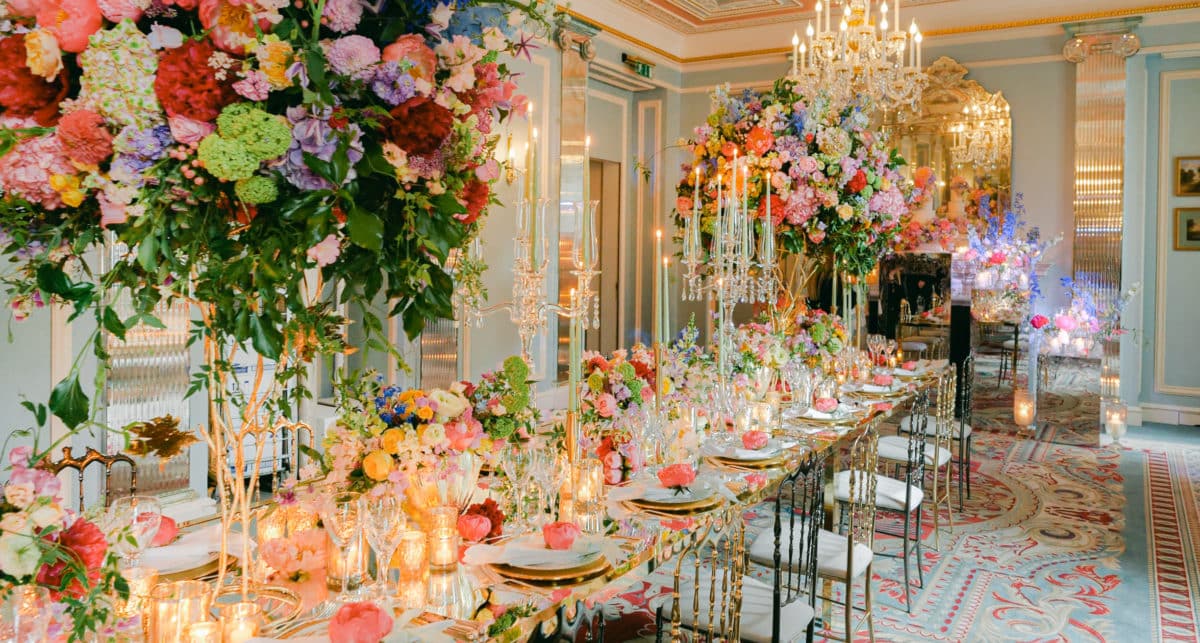 Opulent wedding reception tablescape with oversized colourful floral installations, candlelit tables and gold chiavari chairs in an elegant ballroom — bold wedding styling trend 2026 — HD Moments