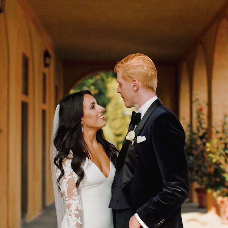 Bride Sam in her Pronovias lace gown and groom Chris in a black tuxedo looking at each other in the arched loggia of Villa Pizzo, Lake Como — photography at their destination wedding in Italy